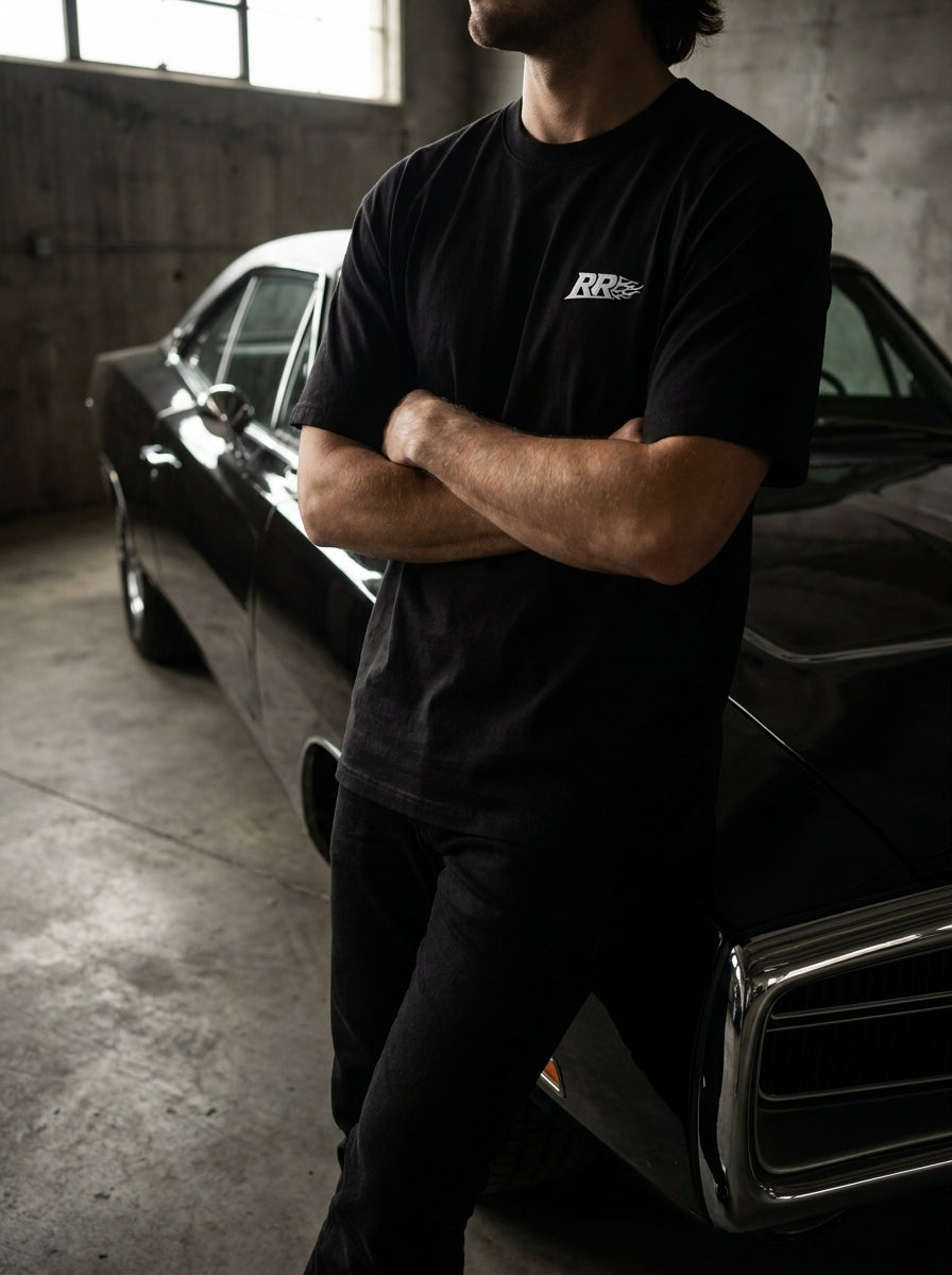 Rowdy Ridez Heavyweight Tee worn leaning on a black muscle car in a garage